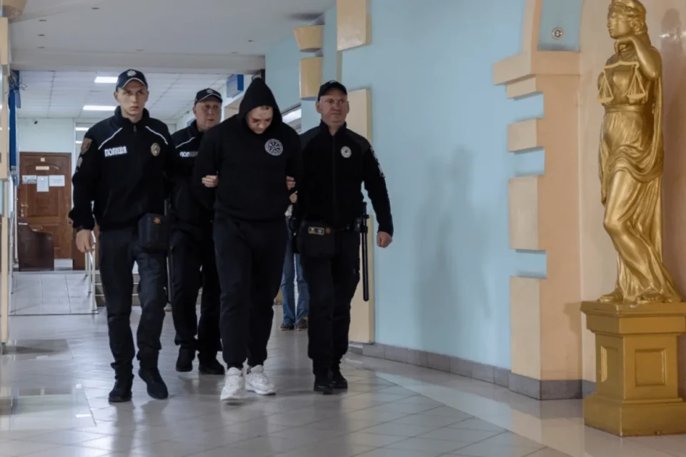 Поліцейські ведуть чоловіка в худі коридором суду біля статуї Феміди