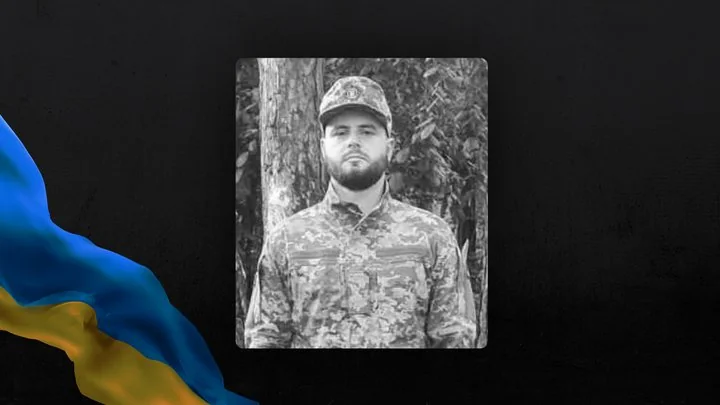 Чорно-білий портрет військового в камуфляжі серед дерев із прапором України