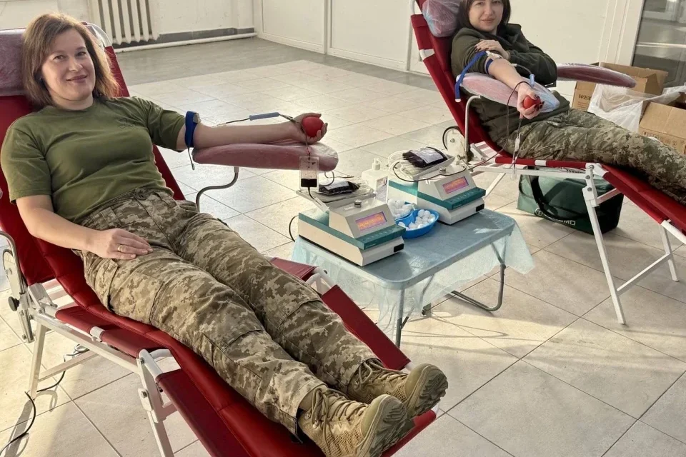 Дві жінки в камуфляжі здають кров на червоних донорських кріслах